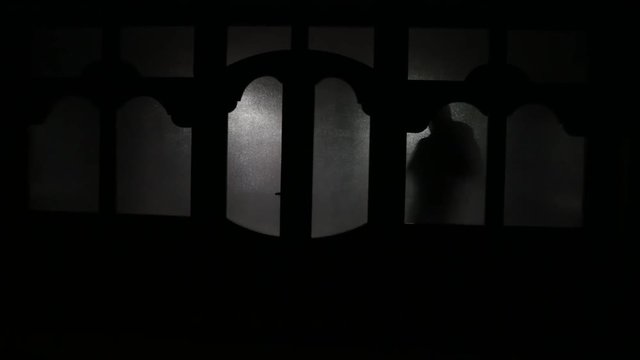Silhouette of an unknown shadow figure on a door through a closed glass door. The silhouette of a human in front of a window at night. Scary scene halloween concept of blurred silhouette of maniac.