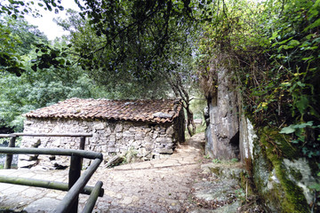 Small old stone farmhouse surrounded by paths with flagstone floor on the side of a mountain with a smooth rock wall in Galicia, Spain.