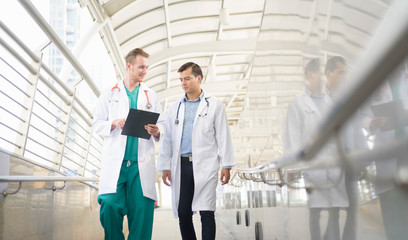 medical doctor professional team talked consult. Two young doctor Caucasian and Asian standing in hospital holding laptop and folder city building background.