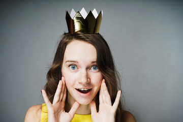 beautiful surprised blue-eyed woman in a yellow dress celebrates Mother's Day, on her head a golden...
