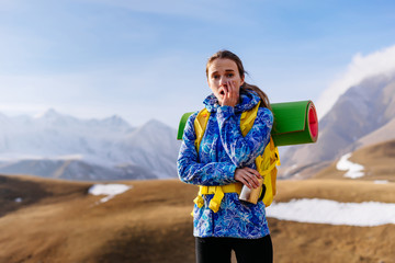 young surprised girl in a blue jacket travels through the Caucasus mountains with a backpack