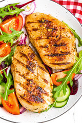 Grilled chicken breast. Fried chicken fillet and fresh vegetable salad of tomatoes, cucumbers and arugula leaves. Chicken meat salad. Healthy food. Flat lay. Top view. White background