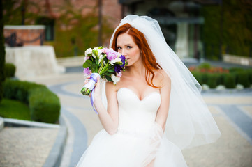 Fototapeta na wymiar Beautiful red haired bride with wedding bouquet walking in the park near castle