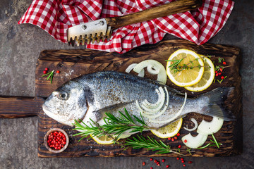 Fresh fish dorado with ingredients for cooking on wooden board. Raw sea bream or dorada fish on dark vintage metal background. Dietary food. Top view