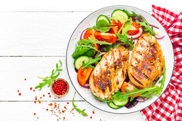 Grilled chicken breast. Fried chicken fillet and fresh vegetable salad of tomatoes, cucumbers and arugula leaves. Chicken meat salad. Healthy food. Flat lay. Top view. White background