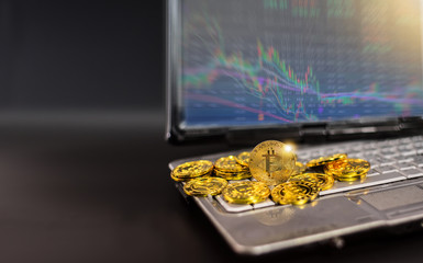 Bitcoin on laptop computer with stock graph screen on black background.