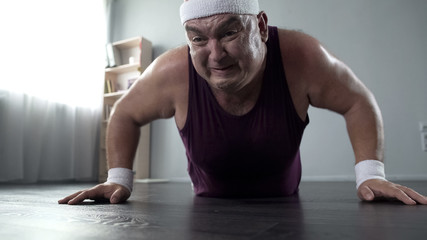 Motivated plump man in his 50s doing push-up with great effort, home training