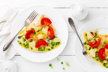 Omelet. Eggs fried. Scrambled eggs with green onion and fresh tomato. Omlette on white plate. Breakfast. Top view. White wooden background