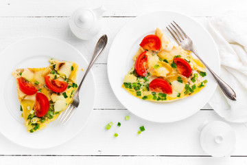 Omelet. Eggs fried. Scrambled eggs with green onion and fresh tomato. Omlette on white plate. Breakfast. Top view. White wooden background