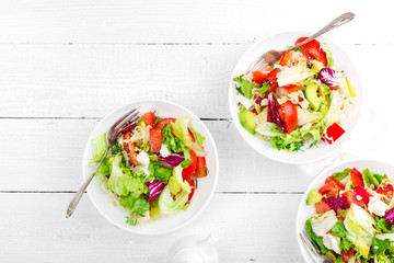 Healthy vegetable salad with fresh greens, lettuce, avocado, tomato, seet pepper and  goat cheese. Delicious and nutritious diet dish for breakfast. Salad bowls on white wooden background