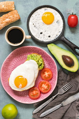 Fried egg with guacamole on toast with tomatoes on grey-blue background.. Breakfast, fried eggs, coffee and pastries. The view from the top.