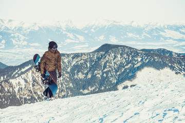 Snowboarder walking at the very top of a mountain with snowboard in his hand