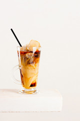Glass of cold coffee or tea with milk and ice cubes on the white table