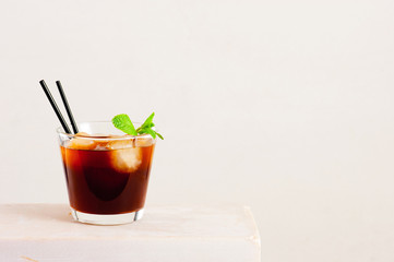 Glass of cold coffee or tea with ice cubes on the white table