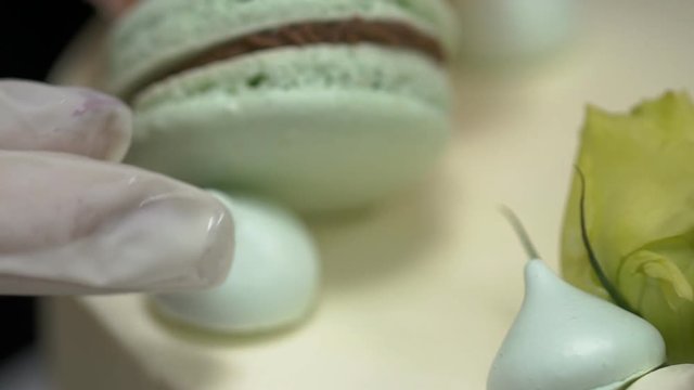 Female confectioner is decorating delightful cake in kitchen in pastry shop. Professional puts meringues on top of tart in cuisine in room. Woman decorates freshly baked mastic cake with light airy