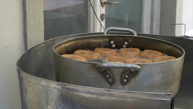 A man frying  donuts in the oil in a big vat, slow motion