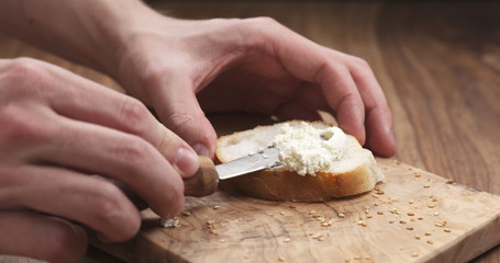 man hands spreading cream cheese on baguette slice on wood board