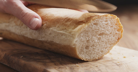 closeup man slicing baguette on wooden board