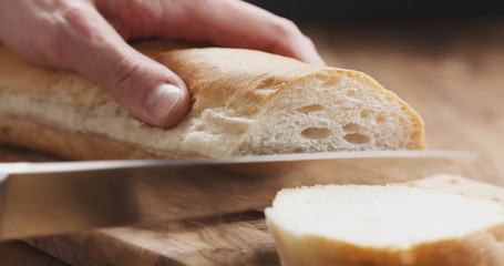 closeup man slicing baguette on wooden board