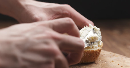 man hands spreading cream cheese on sesame bun on wood board