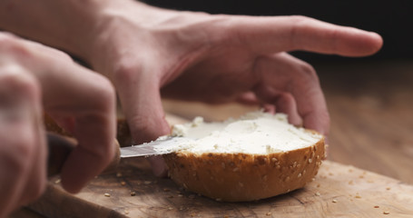 man hands spreading cream cheese on sesame bun on wood board