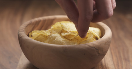 closeup man hand take potato chip from wood bowl