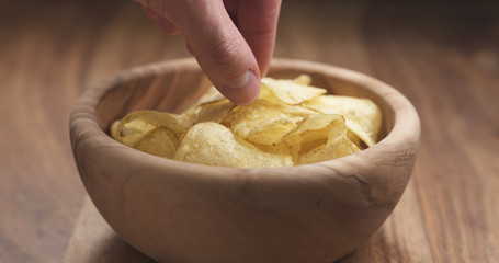 closeup man hand take potato chip from wood bowl