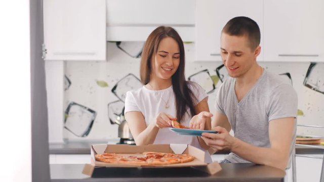 Young happy couple opening box and putting pizza to the dish