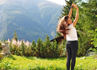 a woman stands with her back and makes gymnastic exercises, stretches up against the background of nature