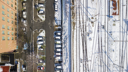 Perpendicular aerial view of the tracks of a subway station. At the side of the tracks there is a city street with parked cars. Everything is covered by snow on this winter day.