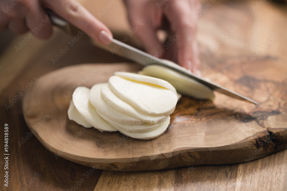 Wall mural female teen hand slicing mozzarella cheese with knife on wooden board