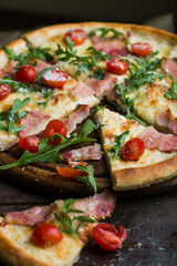 Fresh pizza with tomatoes of cherry, bacon, arugula, parmesan, with olive oil on old trees