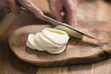 female teen hand slicing mozzarella cheese with knife on wooden board