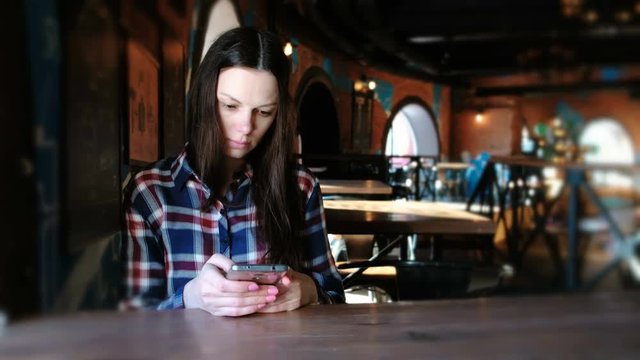 Upset woman sends a message in the phone sitting in a cafe. Dressed in a plaid shirt.