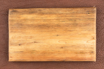 Rectangular board of light wood lies on brown natural leather. Texture of a tree.