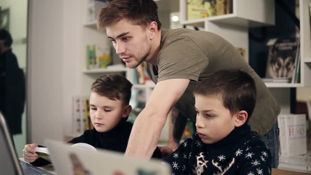 Footage of two boys and their young male programmer teacher in a classroom learning how to use laptop. Alternative education for children.