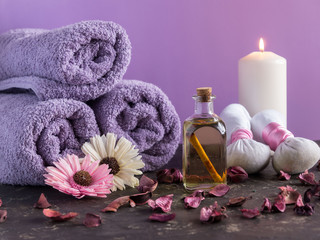 Spa treatment and massage products with towels and oil on stone with violet color background