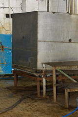 A large old dismantled and rusty tank for collecting milk in an abandoned and destroyed factory against the wall. Destruction and vandalism. Ukraine.