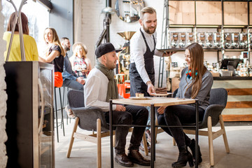Waiter bringing a sweet dessert to a young couple sitting together in the cafe