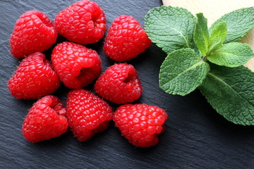 Group of raspberries with few mint leaves on slate board