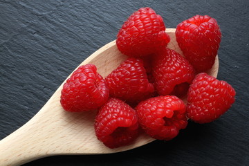 Group of raspberries on wooden kitchen trowel on slate board