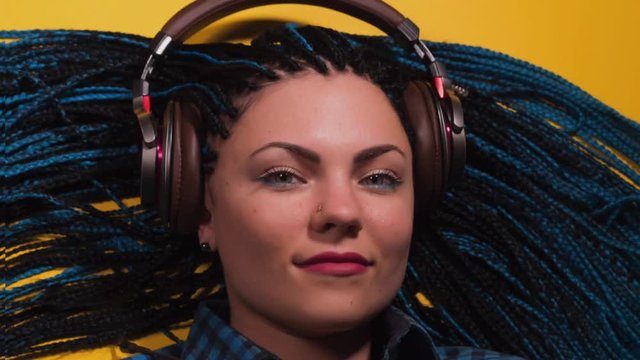 Beautiful young girl with african blue braids is listening to music with headphones and dancing. Stop motion animation. Woman on bright yellow background. Dyed Hair moves.