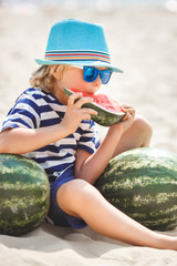 Adorable kid at the sea shore eating juicy watermelon. Cheerful child on summer time on the beach. Cute little boy outdoors