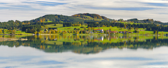panoramic landscape in region Allgaeu with alps mountain range mirroring symmetric in lake