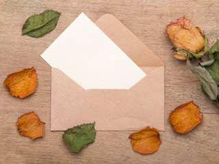 Dried orange roses and envelope on wooden background, copy space