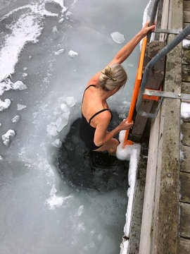 Nice blonde woman descends into hole in the ice in the water for cold winter bathing