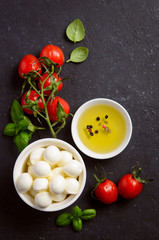 Italian food ingredients – mozzarella, tomatoes, basil and olive oil on black background, top view, flat lay.