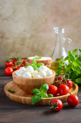 Italian food ingredients – mozzarella, tomatoes, basil and olive oil on rustic wooden table.