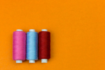 The coils with threads stand vertically on an orange background. A row of coils with bright colored threads standing.