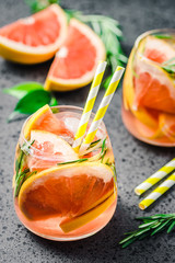 Citrus infused water with grapefruit and rosemary on dark concrete background. Selective focus,...